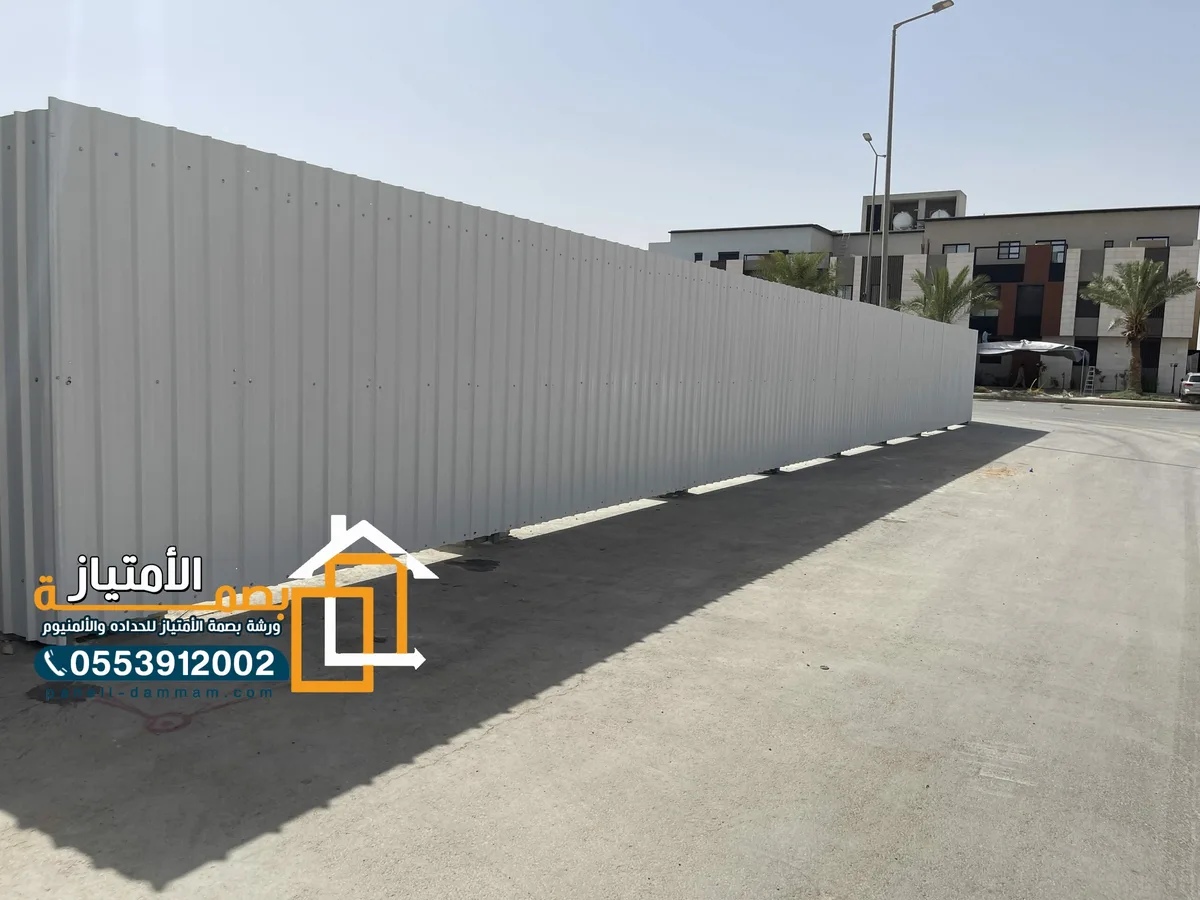 سور تحويش معدني رمادي طويل أمام مبانٍ سكنية في الأحساء