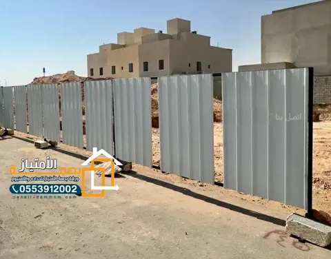 تحويش أرض بألواح معدنية رمادية أمام مبانٍ سكنية قيد الإنشاء في الدمام