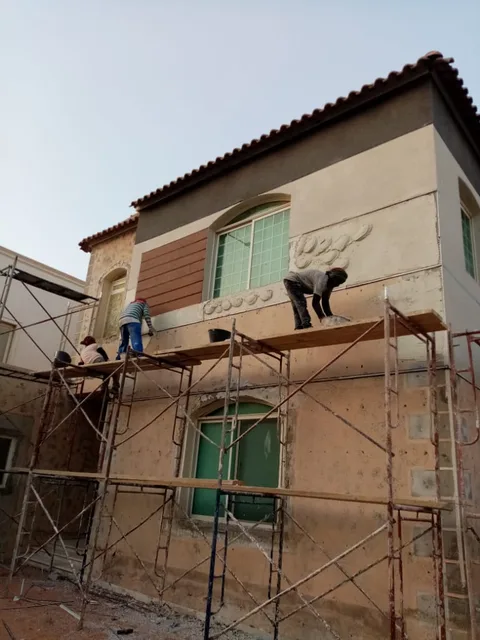 عمال ينفذون ترميم واجهة منزل من فوق السقالات